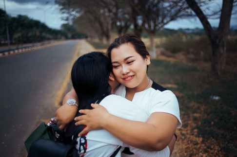 two women hugging each other standing on pathway of the road